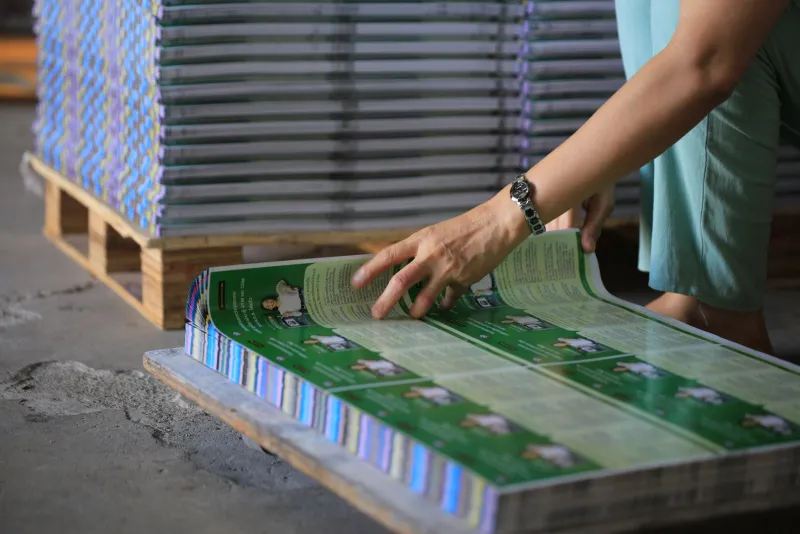 A hand checking freshly printed sheets stacked on a pallet in a print works