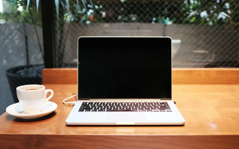 Open laptop beside a cup of coffee on a wooden desk