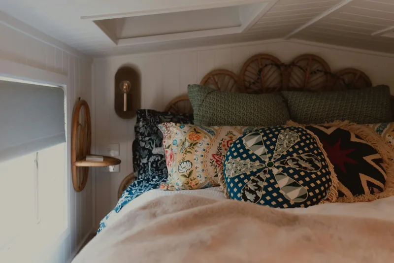 A cosy bed piled with patterned cushions and a soft cream throw under a sloping ceiling