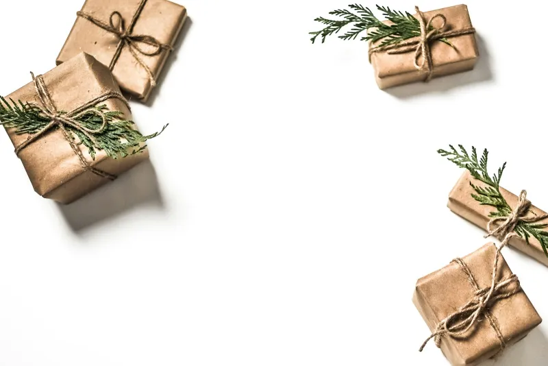 Four small gifts wrapped in brown paper, tied with string and sprigs of greenery, on a white surface