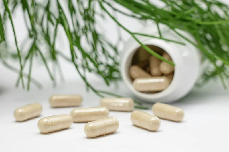 Beige capsules spilling from a white bottle beside green foliage