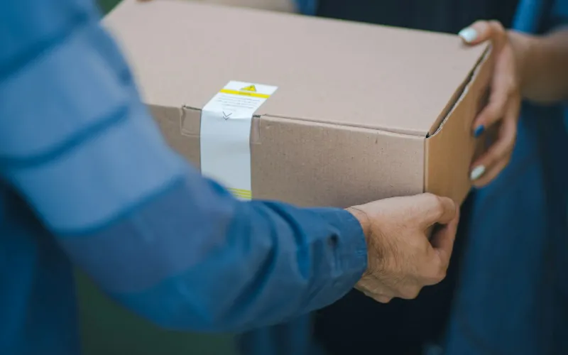 A cardboard parcel being handed over between two people in blue shirts