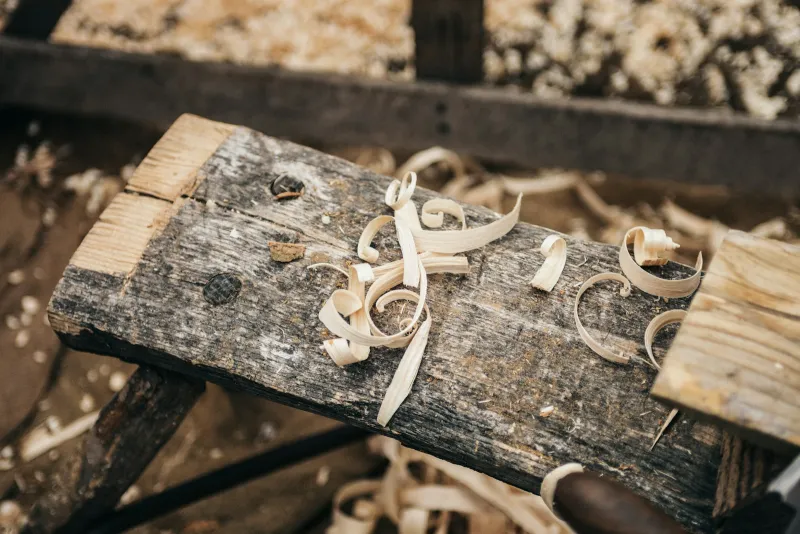 Curled wood shavings on a weathered plank in a woodworking workshop