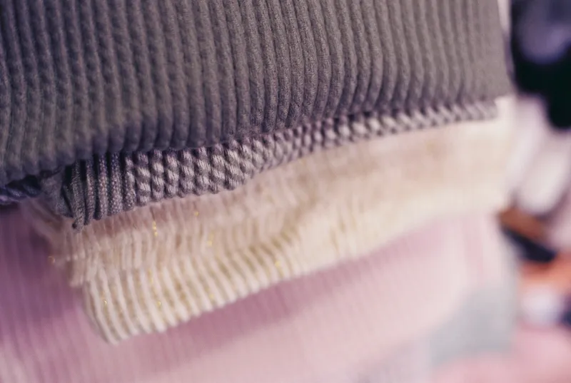 A stack of folded grey, cream and pink knitted jumpers