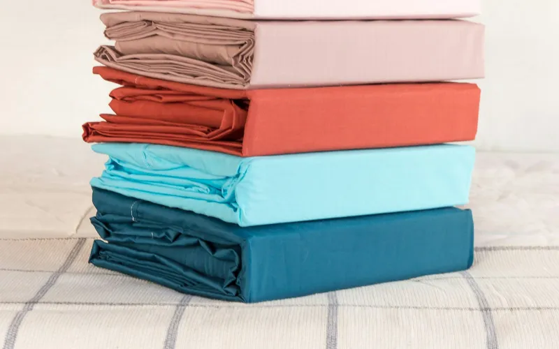 Katruss: sleepwear and loungewear made from rose, aloe and orange fibres A stack of folded fabric in soft colours on a bed