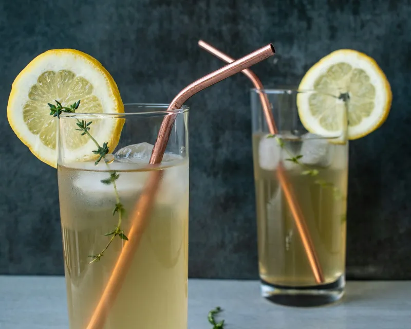 Two tall glasses of iced tea with lemon slices, thyme and copper straws