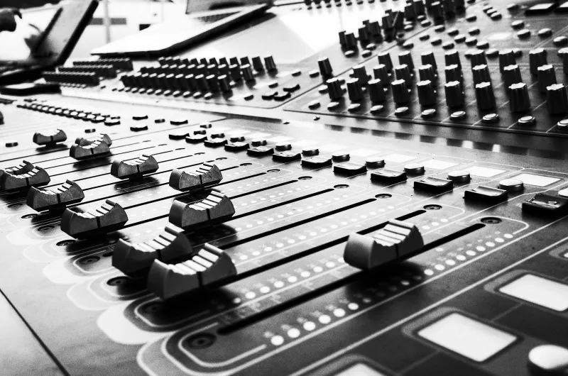 Black and white close-up of faders and knobs on a studio mixing desk