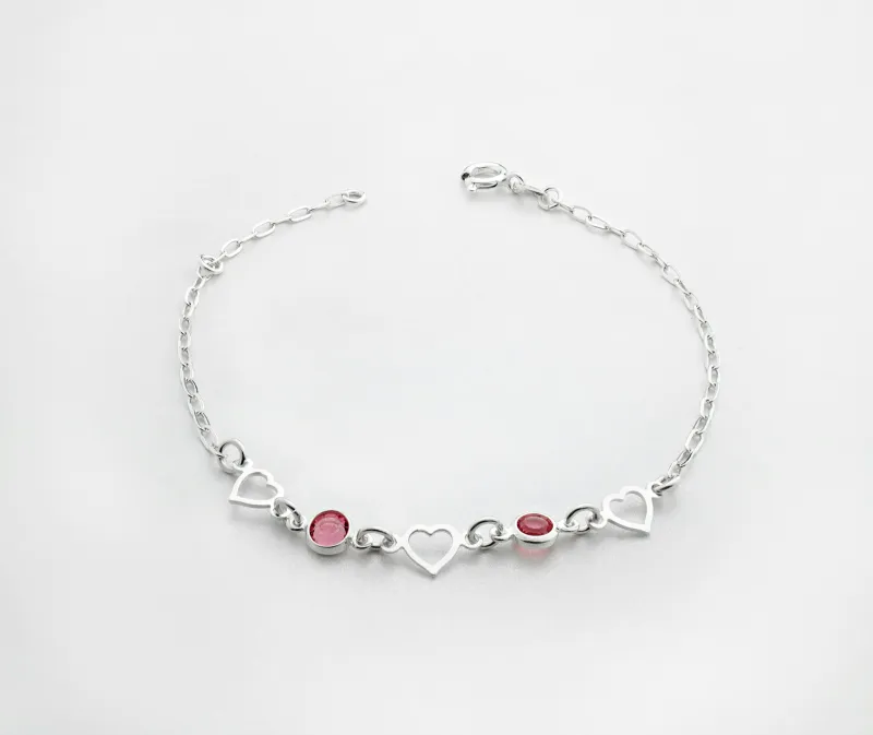 A silver bracelet with heart links and two red stones on a white background