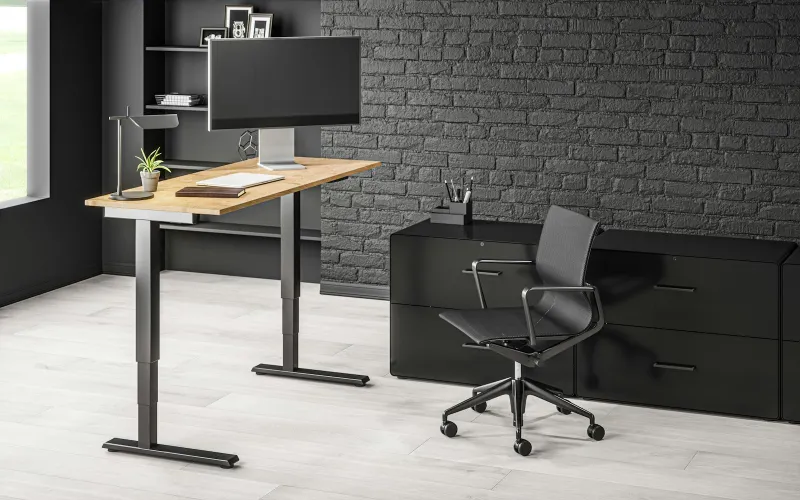 A height-adjustable standing desk with a monitor in a dark home office