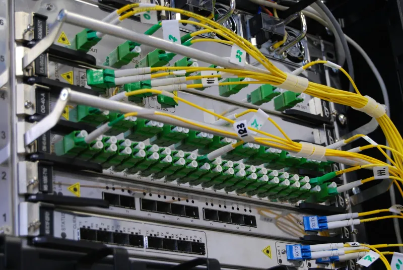 Yellow fibre optic cables plugged into rows of green connectors on network equipment