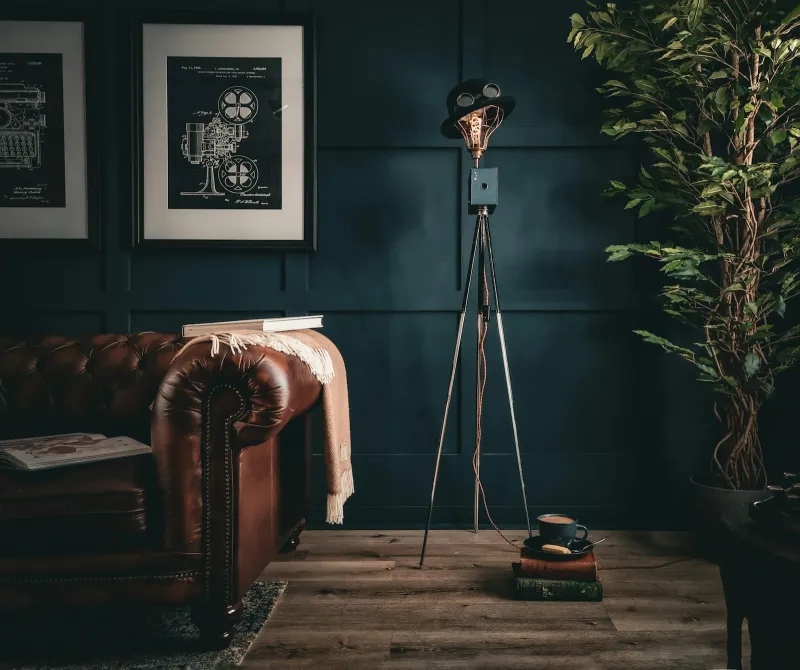 A leather sofa and a tripod floor lamp against a dark panelled wall