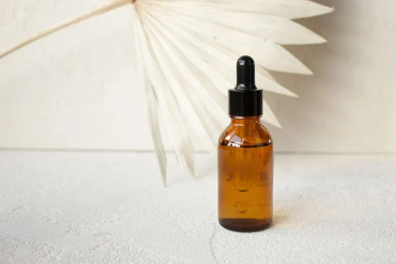 An amber glass dropper bottle in front of a dried white palm leaf