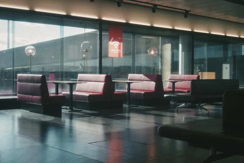Empty airport lounge seating with red booths beside large windows