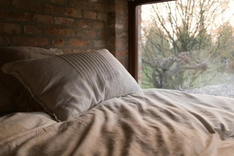 Pillow and rumpled linen duvet on a bed beside a large window