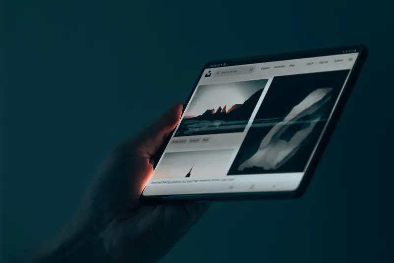 A hand holding a tablet showing a photo gallery against a dark background