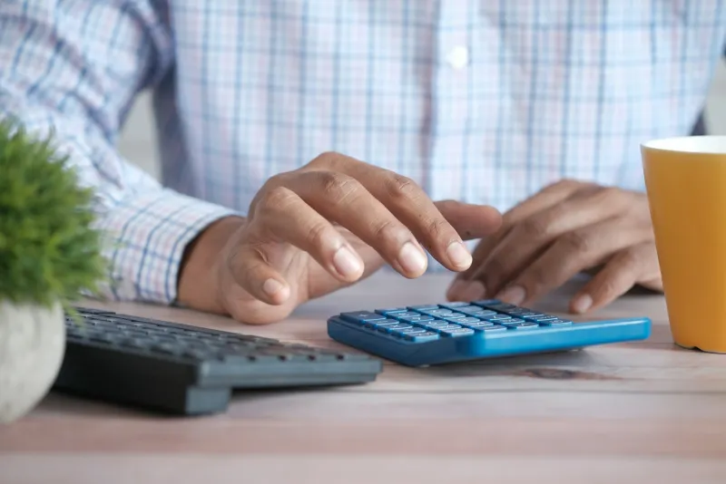 Person using a calculator at a desk beside a keyboard and a mug