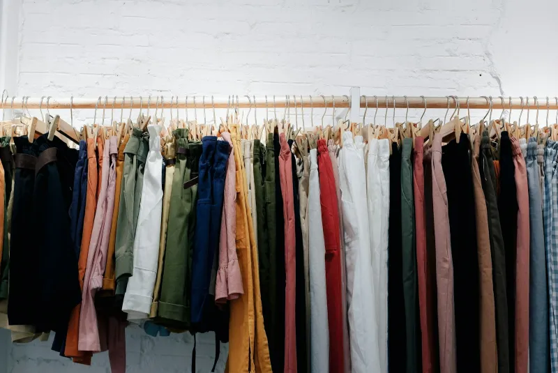 Rail of colourful trousers and shorts on wooden hangers against a white brick wall