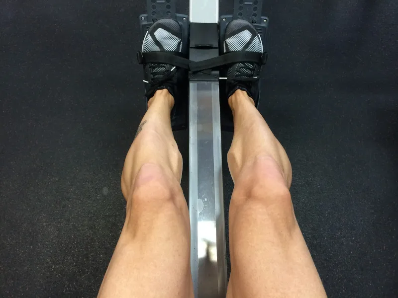 Looking down at legs and trainers strapped into the footrests of a rowing machine