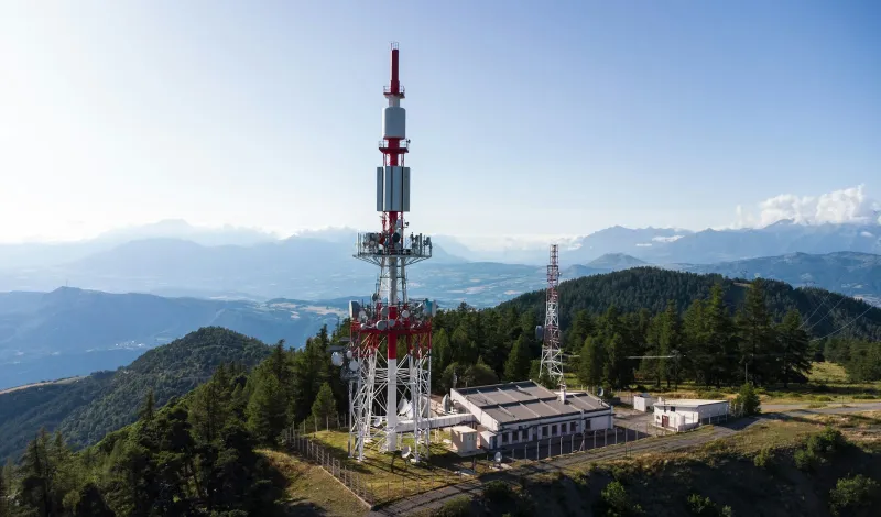Radio mast on a forested hilltop with mountains behind
