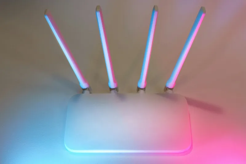 A white wireless router with four upright aerials lit in soft blue and pink light