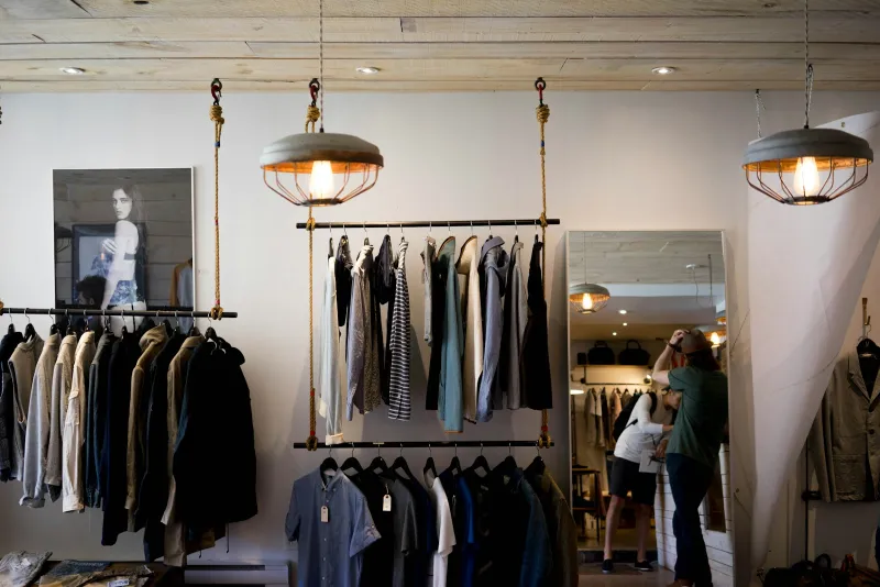 Rails of coats and shirts hanging in a bright clothing boutique with pendant lamps