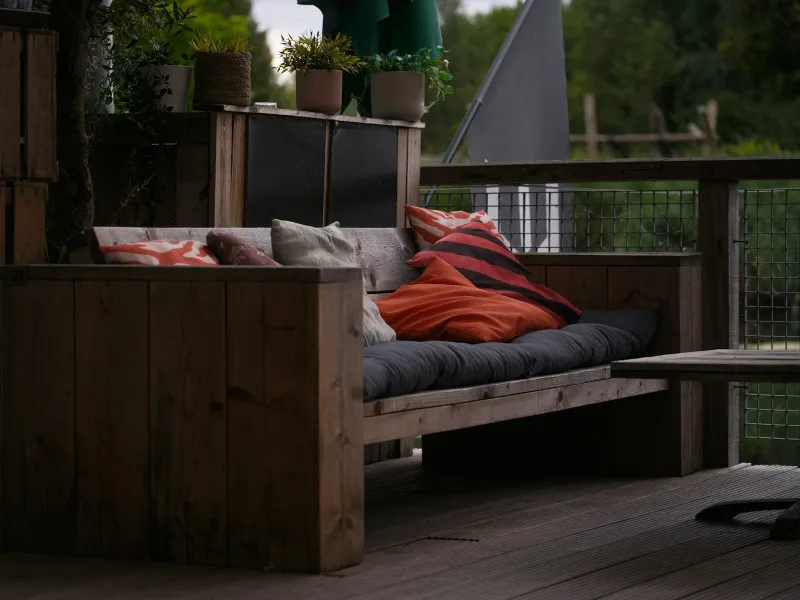 Wooden outdoor sofa with grey seat cushions and colourful scatter cushions on a garden deck