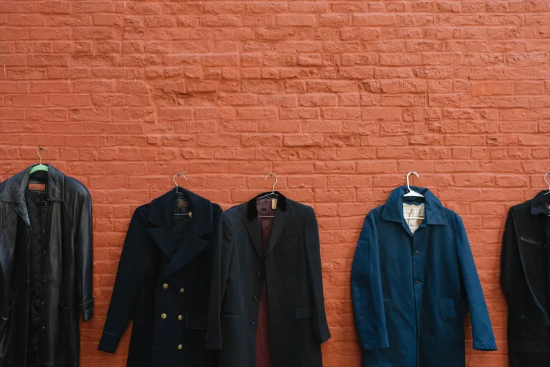 A row of men's coats on hangers against a red brick wall