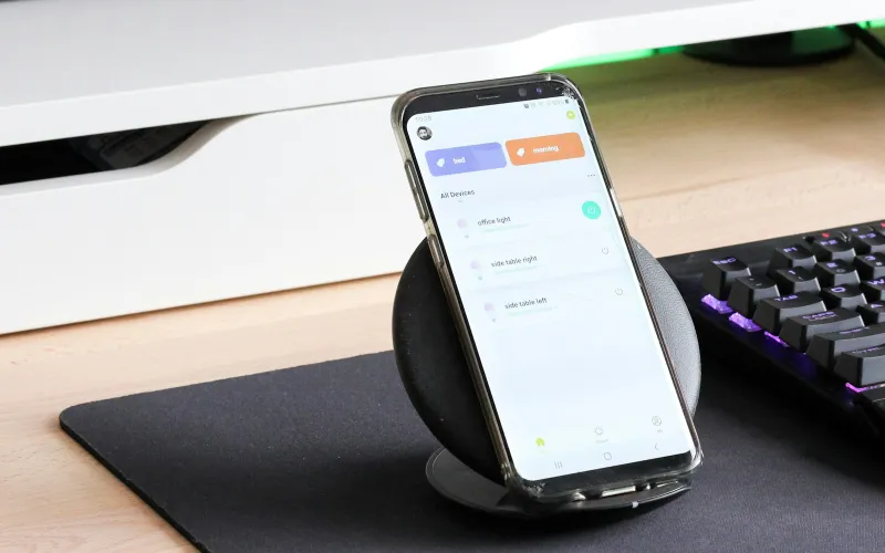 A smartphone standing on a wireless charging stand on a desk next to a keyboard