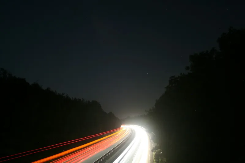 Long-exposure light trails on a motorway at night between dark trees