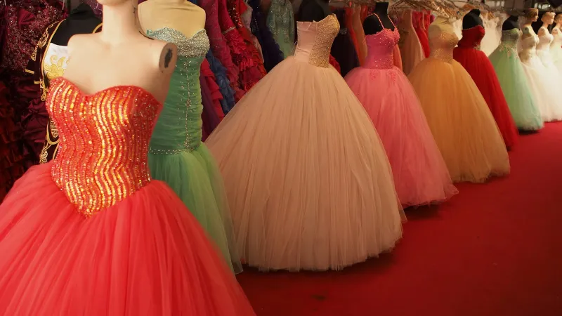 A row of colourful ball gowns with sequinned bodices on mannequins along a red carpet
