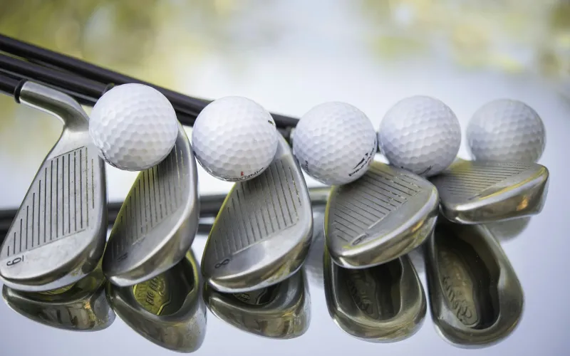 A row of golf irons with golf balls resting on the club heads