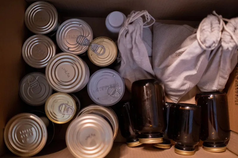 A cardboard box packed with tins, jars and cloth bags of dried food, seen from above
