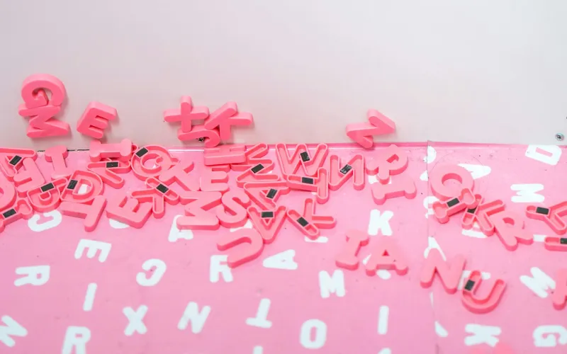 Pink magnetic alphabet letters scattered across a pink board