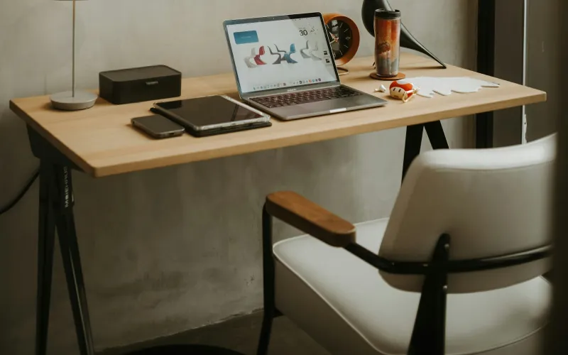 A laptop and tablet on a tidy wooden desk beside a white chair