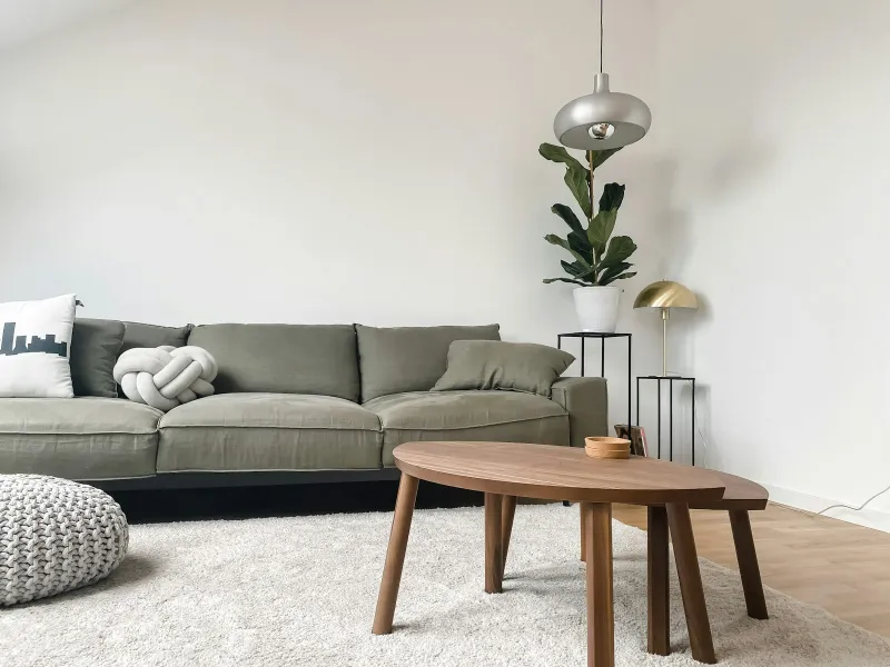 Living room with a green sofa, wooden coffee tables, a rug and a potted plant