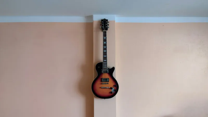A sunburst electric guitar hanging on a peach-coloured wall