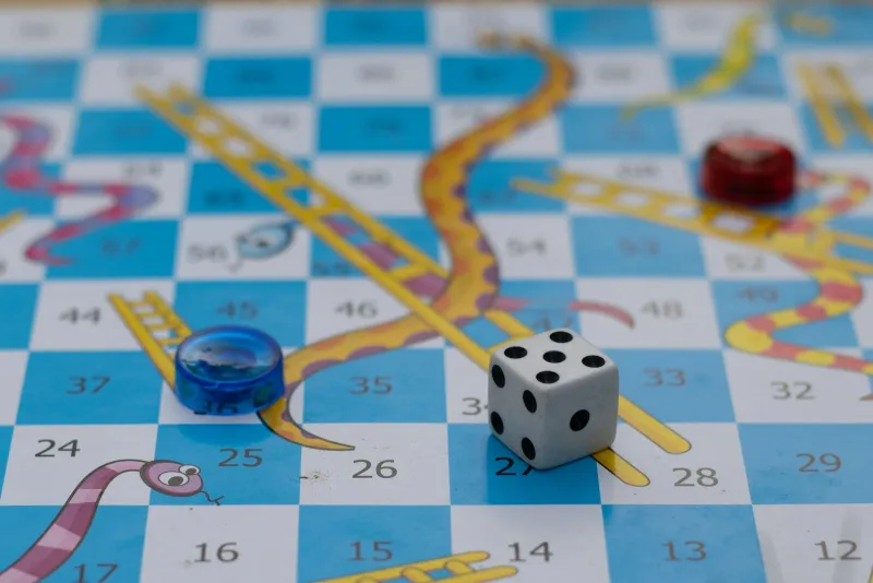 A dice and two counters on a snakes and ladders board