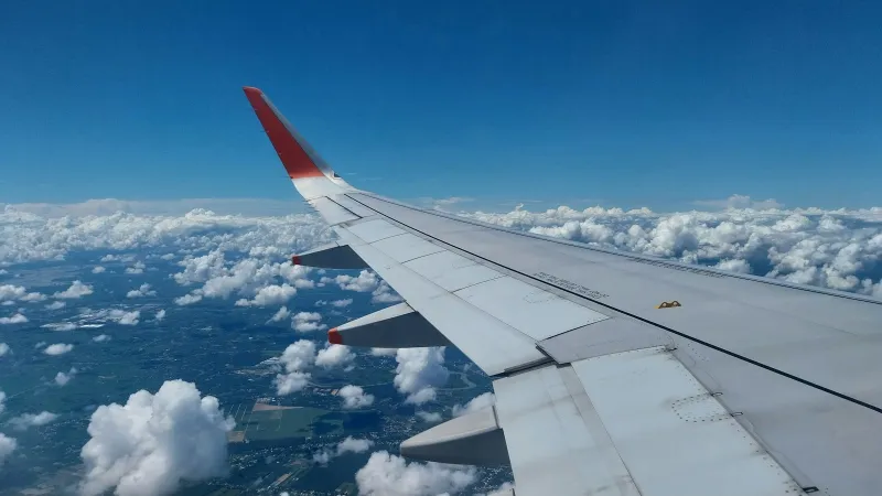 Ovago: flight bookings with phone agents and WhatsApp support An aircraft wing above scattered white clouds and fields