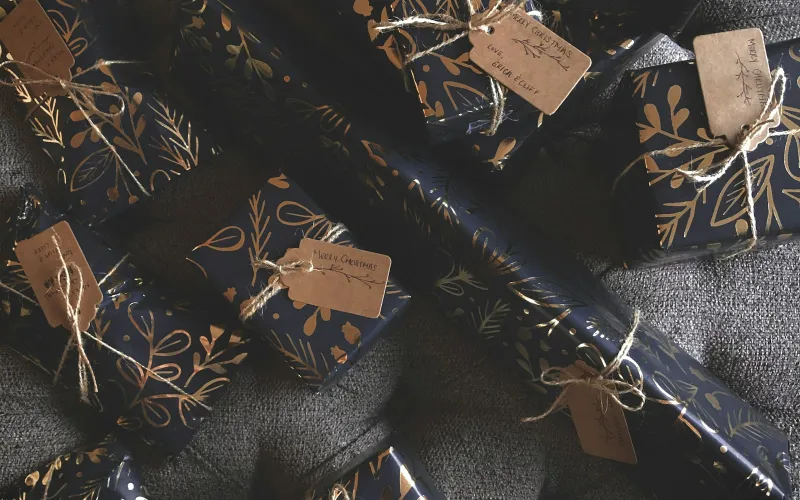 Presents in navy and gold wrapping paper tied with twine and handwritten Christmas tags