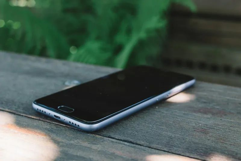 Phones Direct: refurbished iPhones and Samsung phones with a 12-month warranty A smartphone lying face up on a weathered wooden table with greenery behind