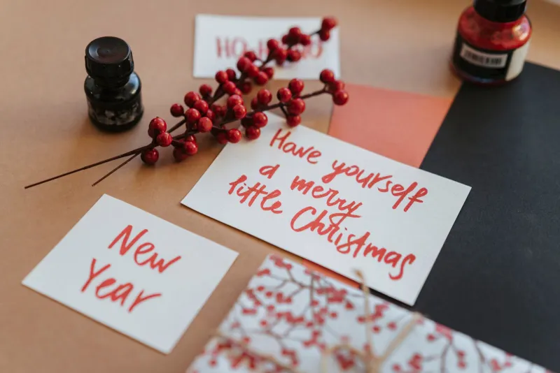 Handwritten Christmas and New Year cards on brown paper with a sprig of red berries and bottles of ink