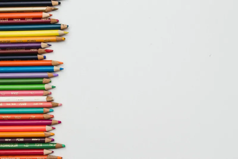 Row of coloured pencils lined up on white paper