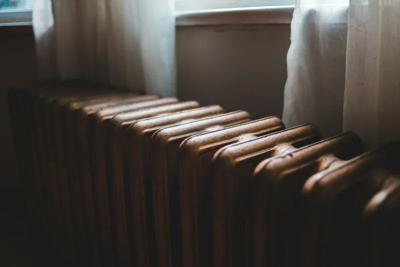 Old cast iron radiator beneath a curtained window