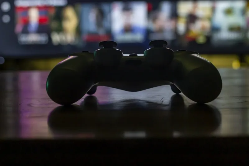 Silhouette of a games controller on a coffee table in front of a blurred TV screen