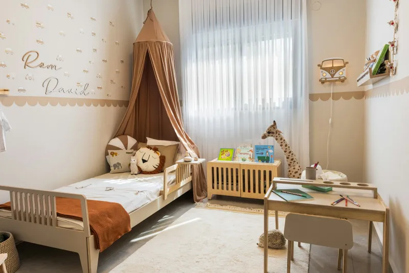 Child's bedroom with a canopy over the bed, cushions, a small desk and a toy giraffe