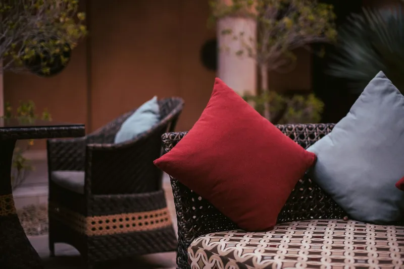 Dark woven rattan sofa and armchair with red and blue cushions on a garden patio