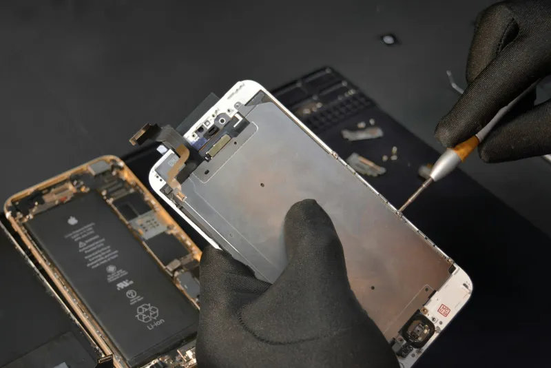 Gloved hands using a screwdriver to take apart a smartphone on a repair mat