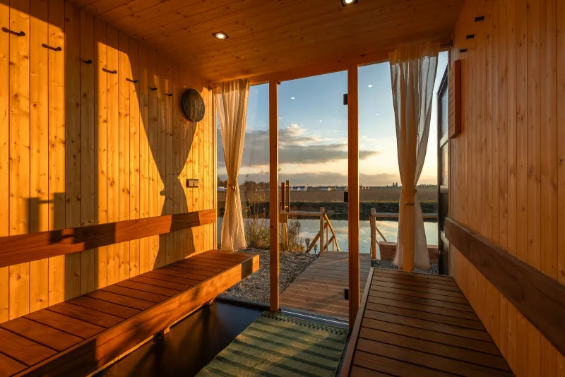 Wooden sauna interior with benches and glass doors opening onto a lake at sunset