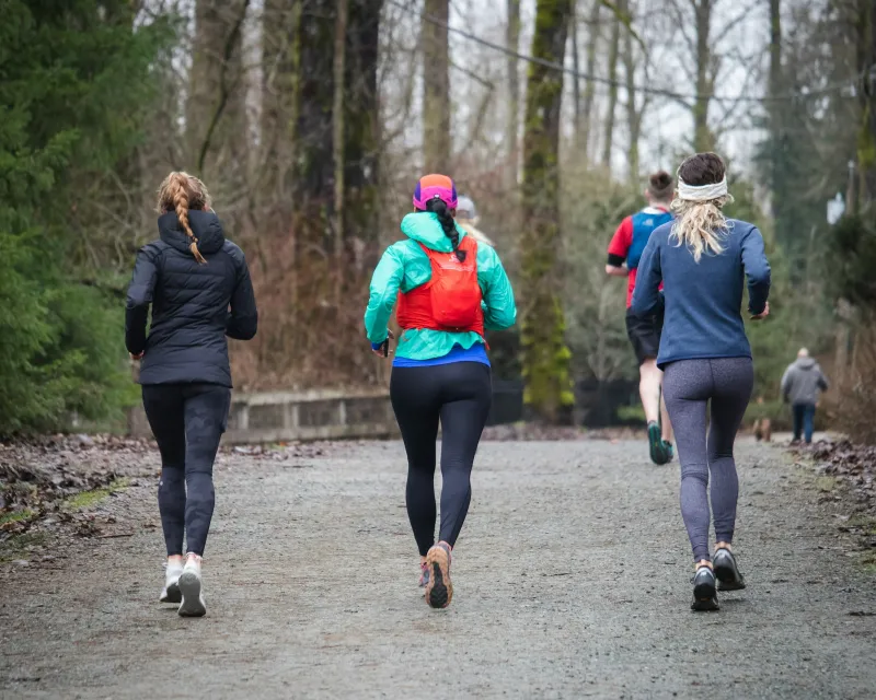 Runners in leggings and jackets jogging away along a woodland trail