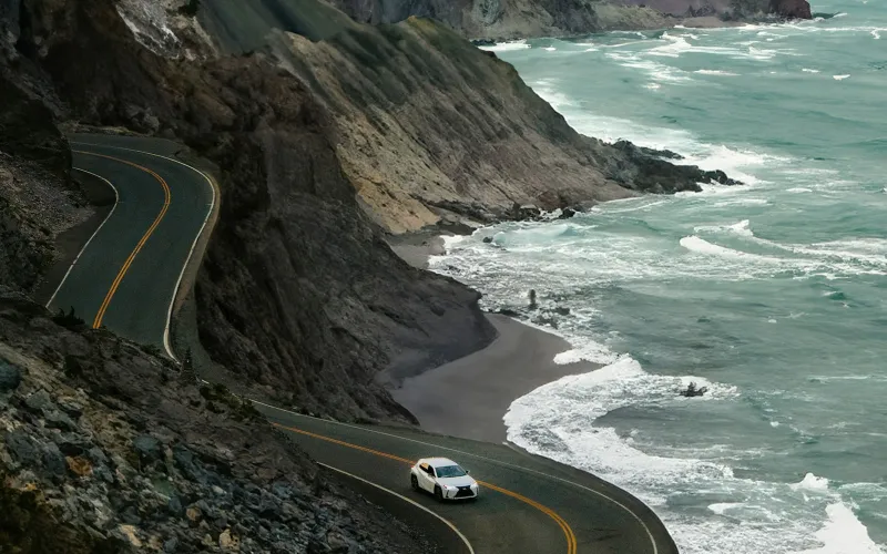 White car on a winding cliff road above a rocky beach and rough sea